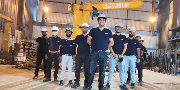 Venus Engineering Works service team in VENU polo shirts and white hard hats, standing under the Demag jib crane at the Kuha works.