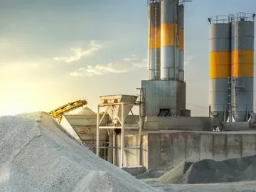 Cement plant silos and conveyor above a stockpile of raw material