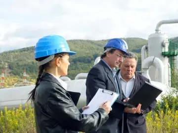 Engineers in hard hats reviewing drawings outside a treatment plant