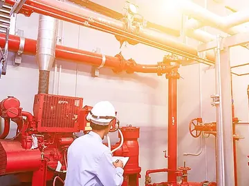 Engineer checking a fire pump room with red sprinkler mains and valves